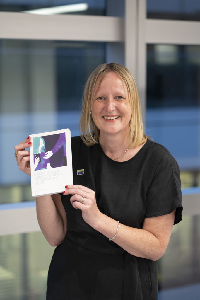 Dr Nicola Sharp-Jeffs holds a printed copy of Understanding and Responding to Economic Abuse